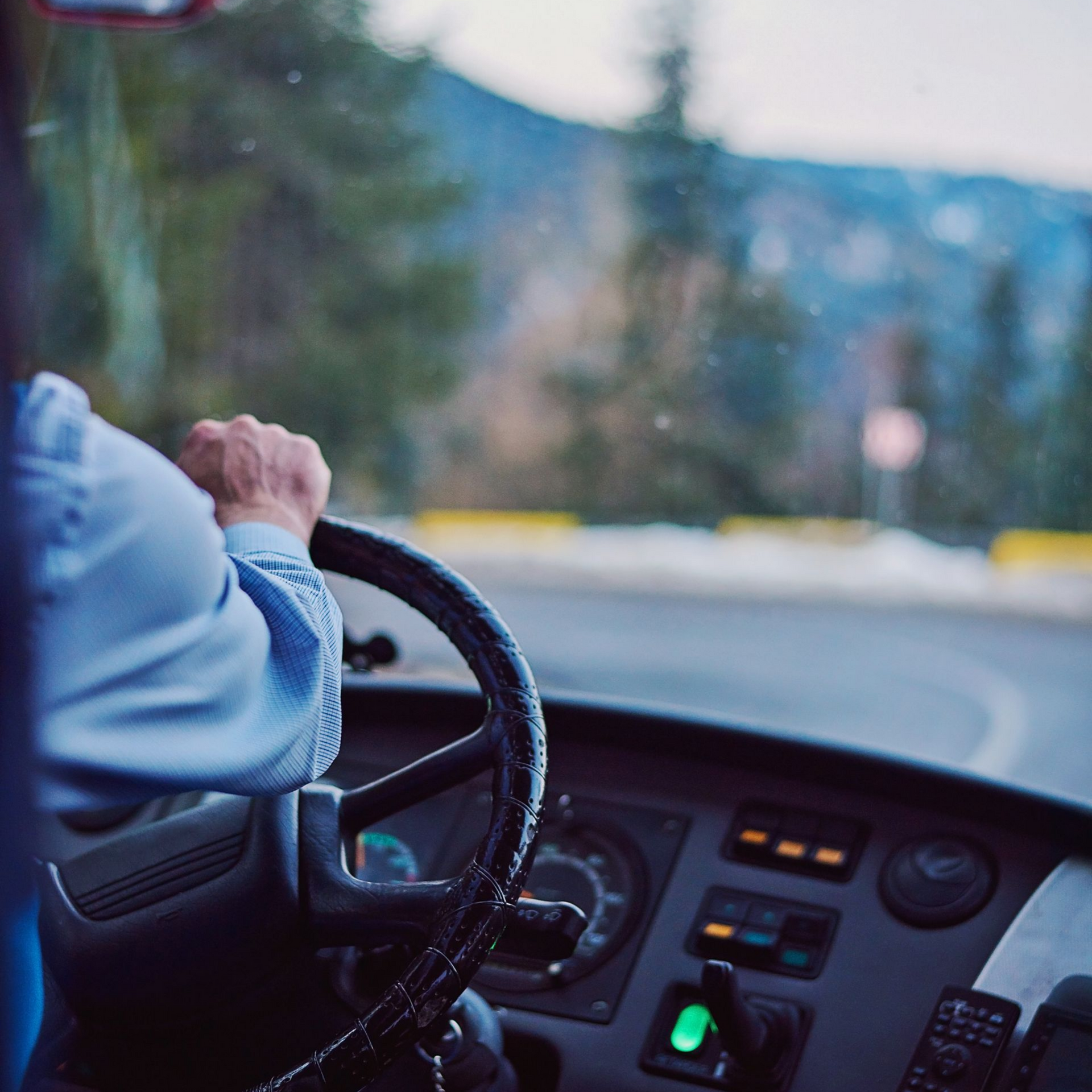 Chauffeur au volant d'un bus dans un paysage de montagnes.