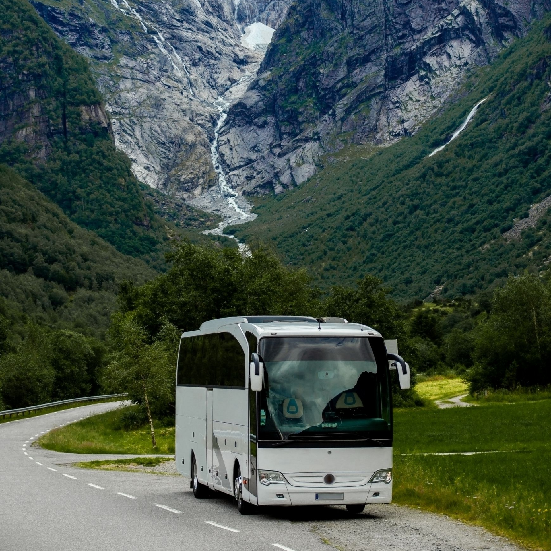 Un bus touristique blanc circule sur une route sinueuse au milieu d'un paysage montagneux avec une cascade et une végétation luxuriante.