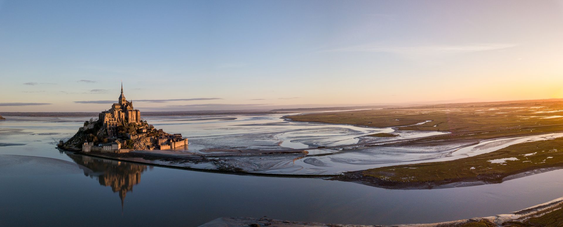 Vue du Mont Saint-Michel, île normande accessible à marée basse, se reflétant dans les eaux calmes, au lever du soleil.