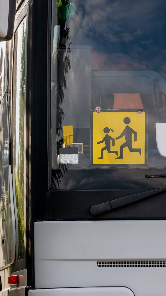 Autobus scolaire avec un panneau attention enfants de couleur jaune derrière le pare-brise.