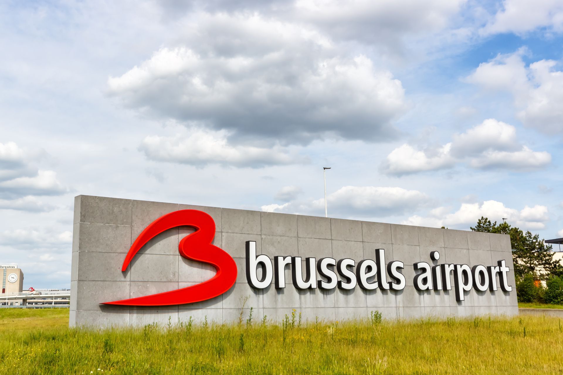 Panneau de l'aéroport de Bruxelles avec logo rouge sur un bloc de béton.