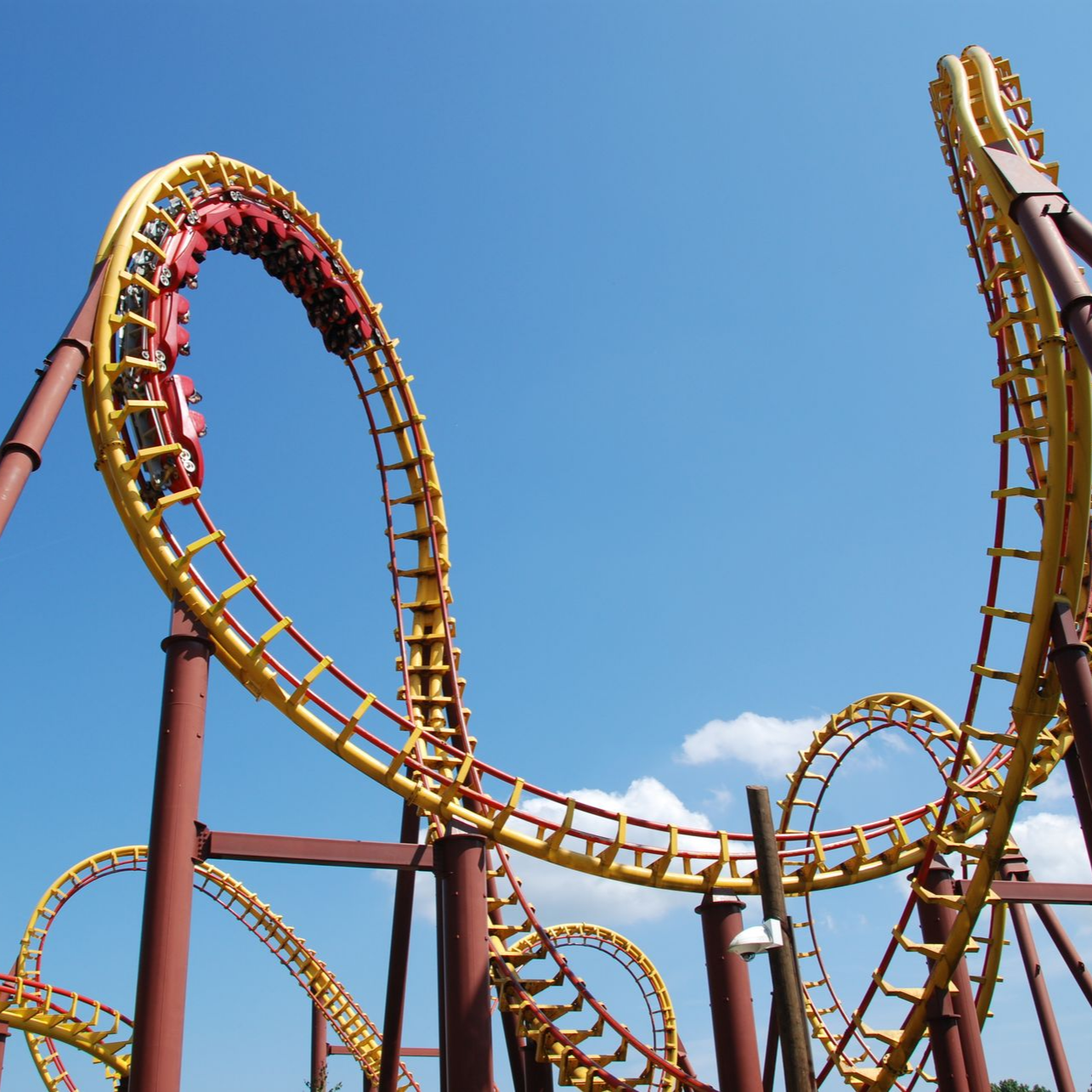 Montagnes russes avec des rails jaunes et des wagons rouges sur fond de ciel bleu.