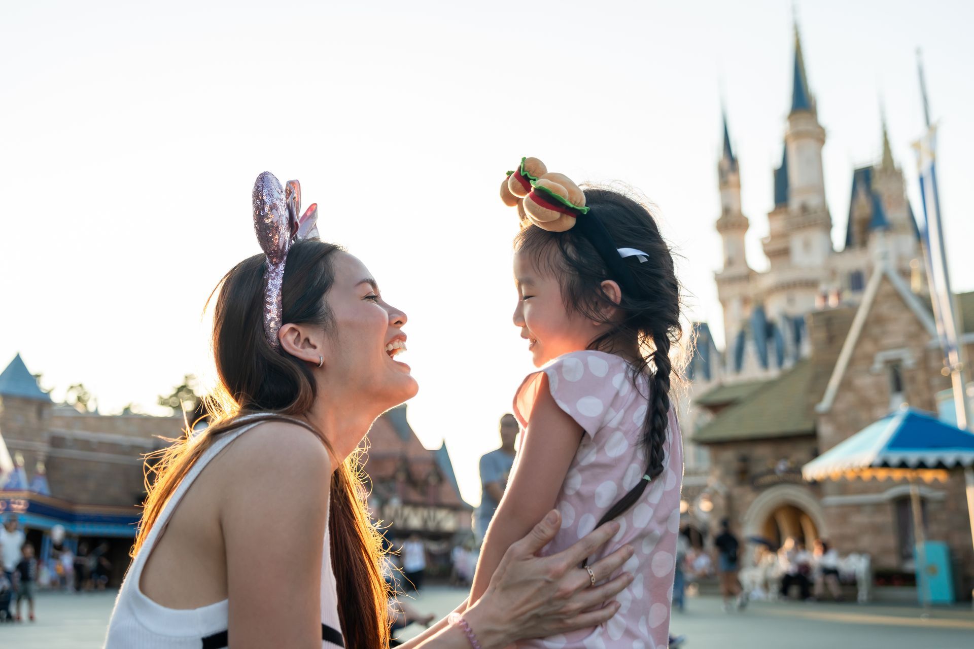 Une mère et son enfant avec le sourire portant des oreilles de Mickey devant un château dans un parc d'attractions.