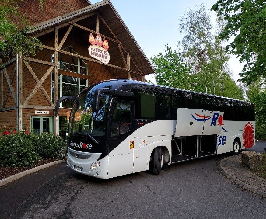 Un autocar de tourisme blanc des Voyages Rose est stationné devant un hôtel du Parc Astérix.