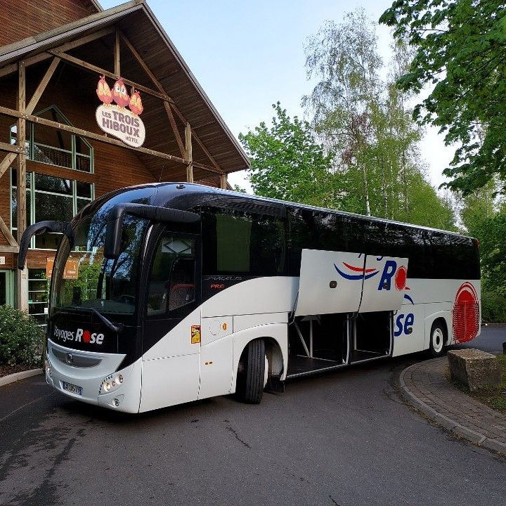 Un autocar de tourisme blanc des Voyages Rose est stationné devant un hôtel du Parc Astérix.