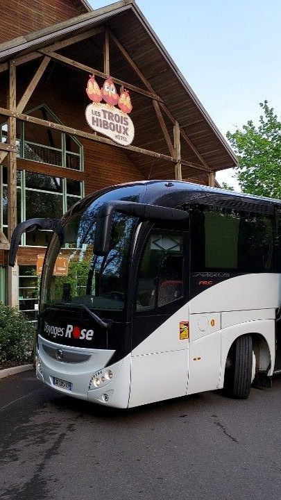 Un autocar de tourisme blanc des Voyages Rose est stationné devant un hôtel du Parc Astérix.