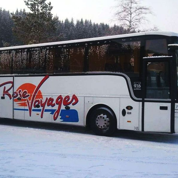 Un autocar blanc Voyages Rose est stationné dans un paysage enneigé.