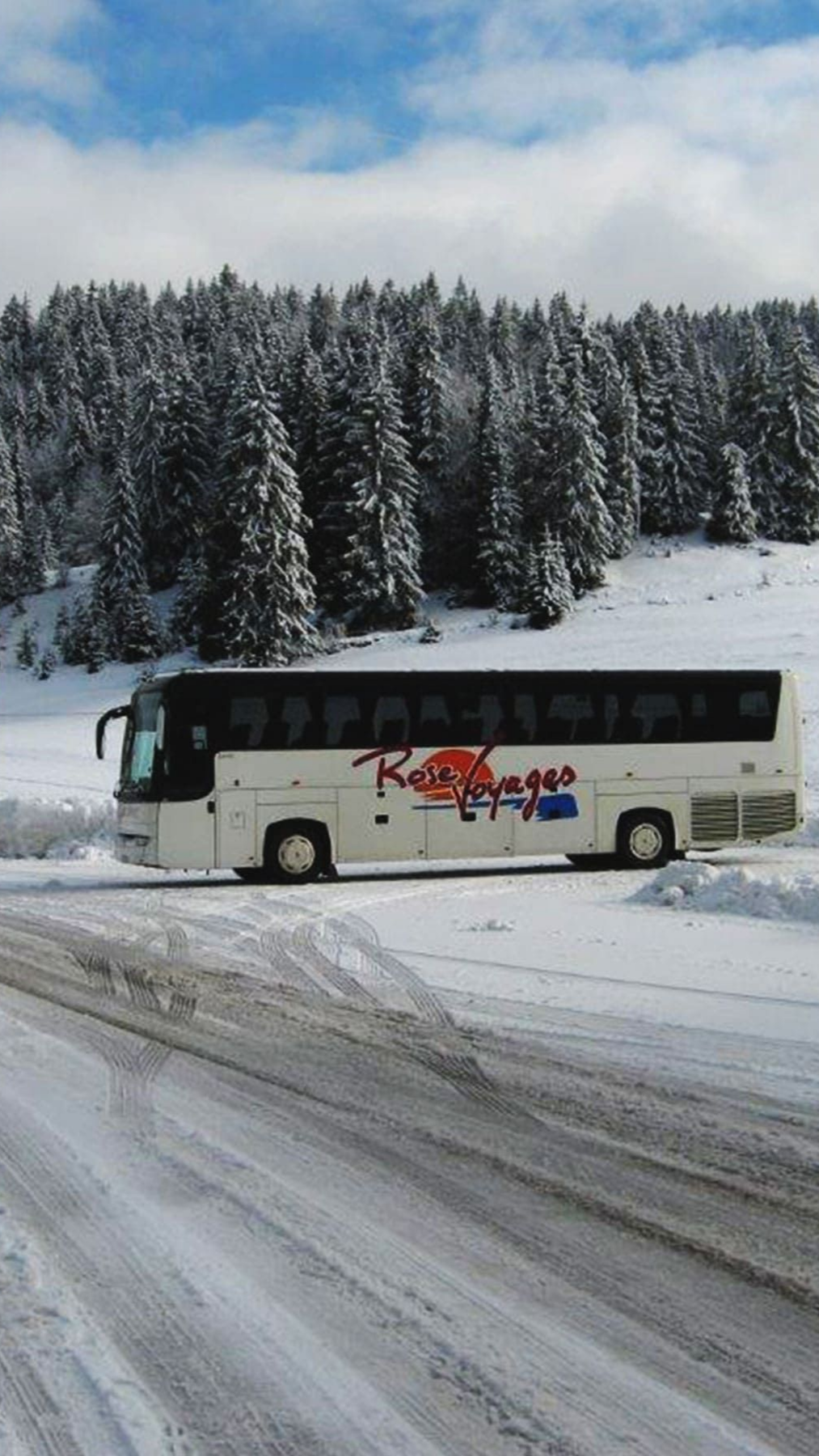 Autocar blanc de tourisme stationné sur une route enneigée.