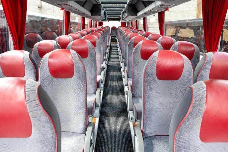Intérieur d'un bus vide avec des rangées de sièges gris et rouges, des rideaux rouges et une allée centrale.