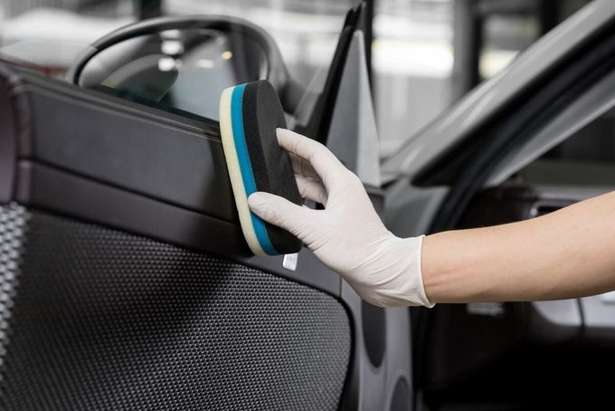 Una persona está limpiando la puerta de un coche con una esponja.