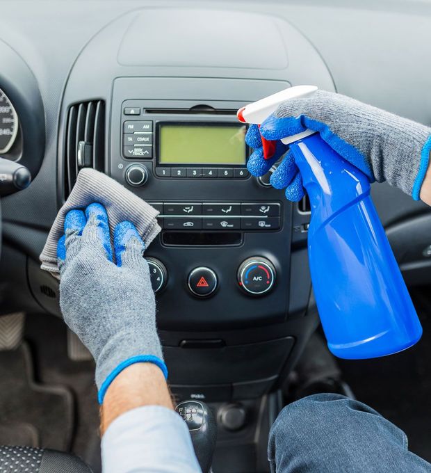 Una persona está limpiando el tablero de un automóvil con un paño y una botella de spray.