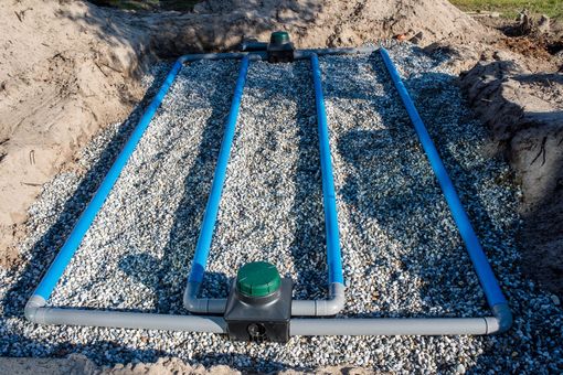 Lit de gravier à cadre bleu avec un arroseur/vanne de jardin vert au centre, installé dans une zone de terre.