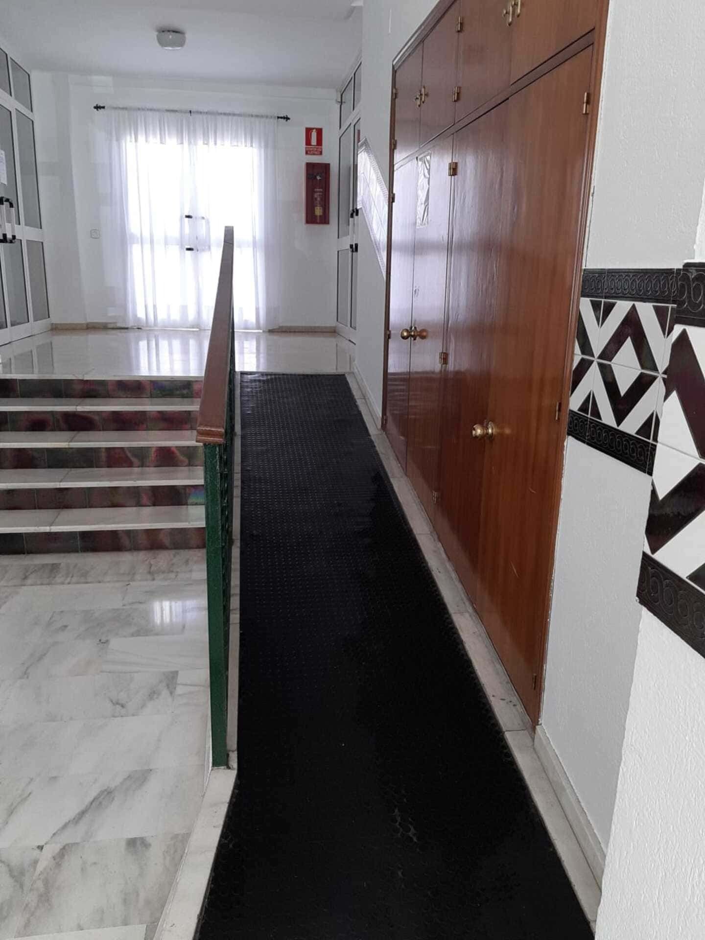 Un largo pasillo con escaleras y una alfombra negra.