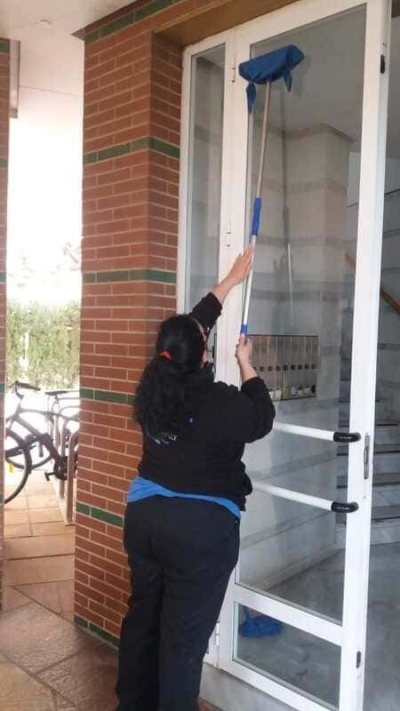 Una mujer está limpiando una puerta de vidrio con un trapeador.