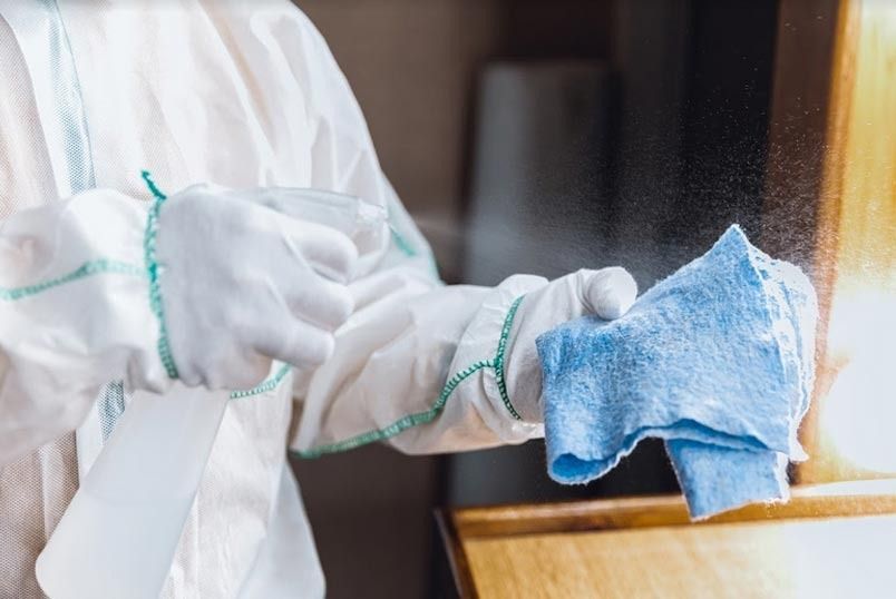 Una persona con un traje de protección está limpiando una mesa con un paño azul.