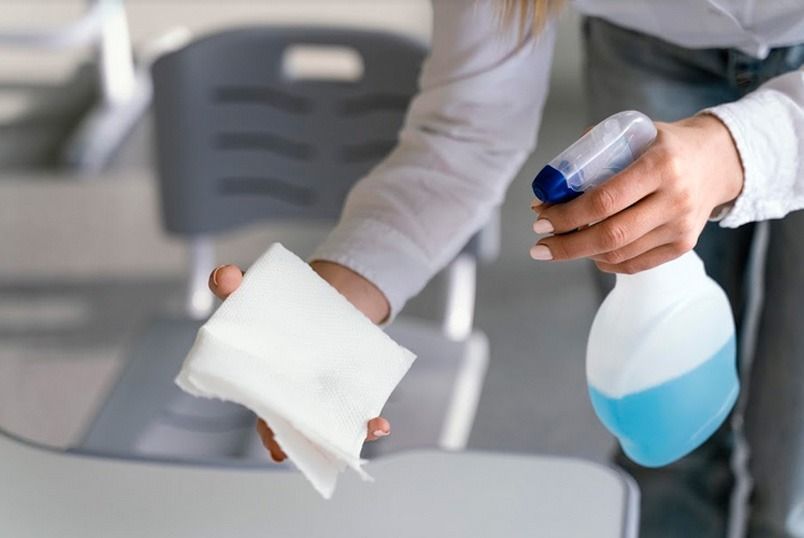 Una mujer está limpiando una mesa con una botella de spray y una servilleta.