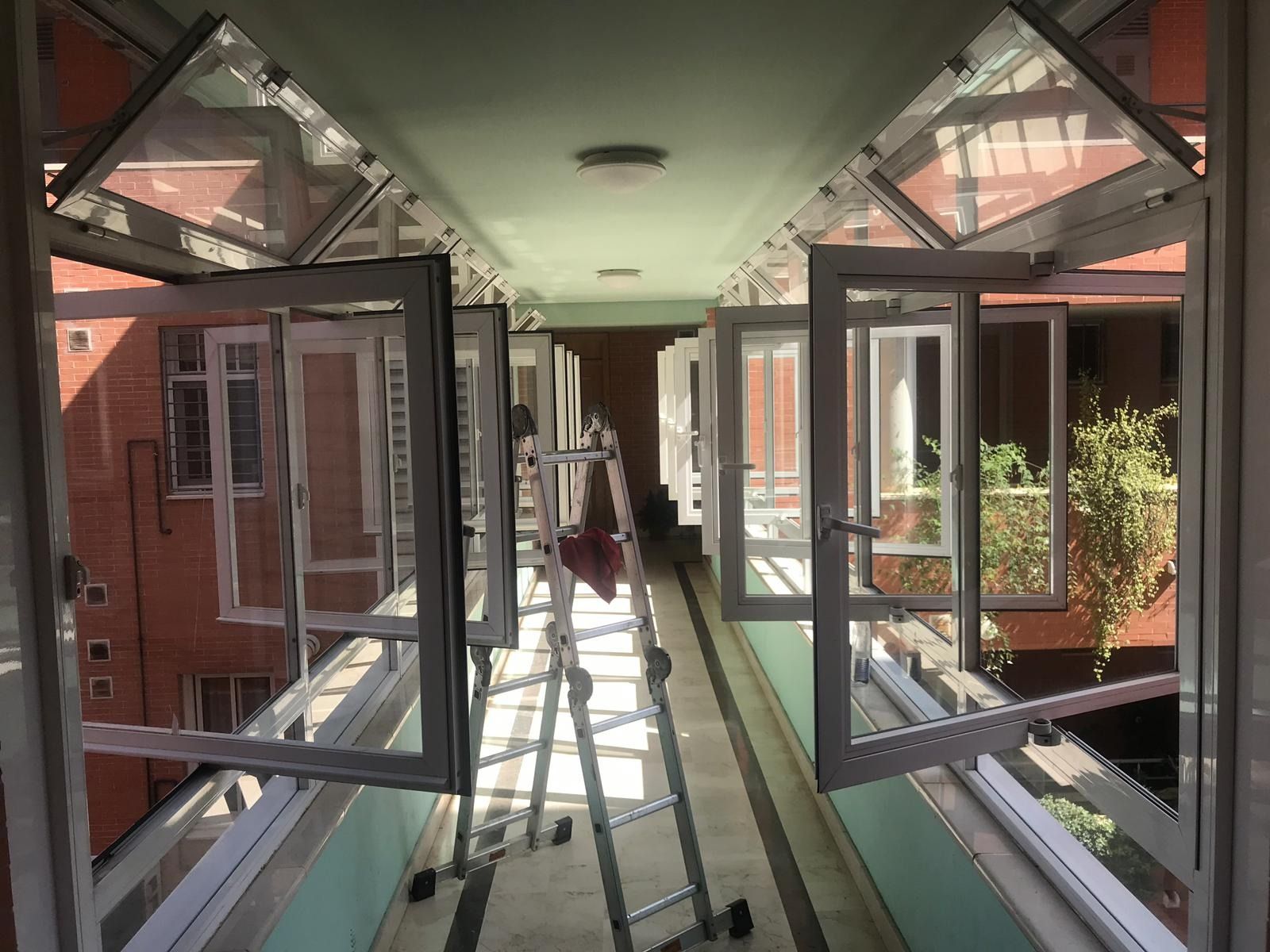 Un largo pasillo con una escalera y muchas ventanas abiertas.