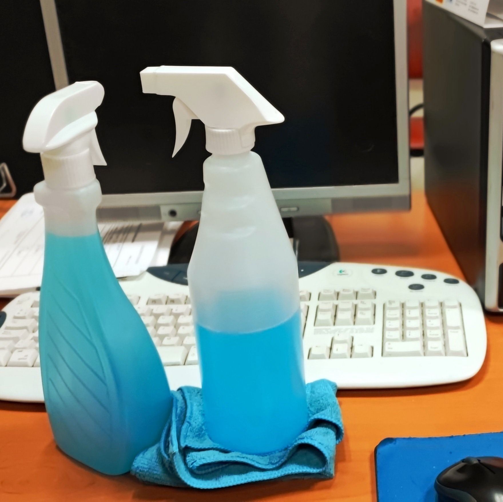 Dos botellas de spray con líquido azul se encuentran sobre un escritorio frente a una computadora.
