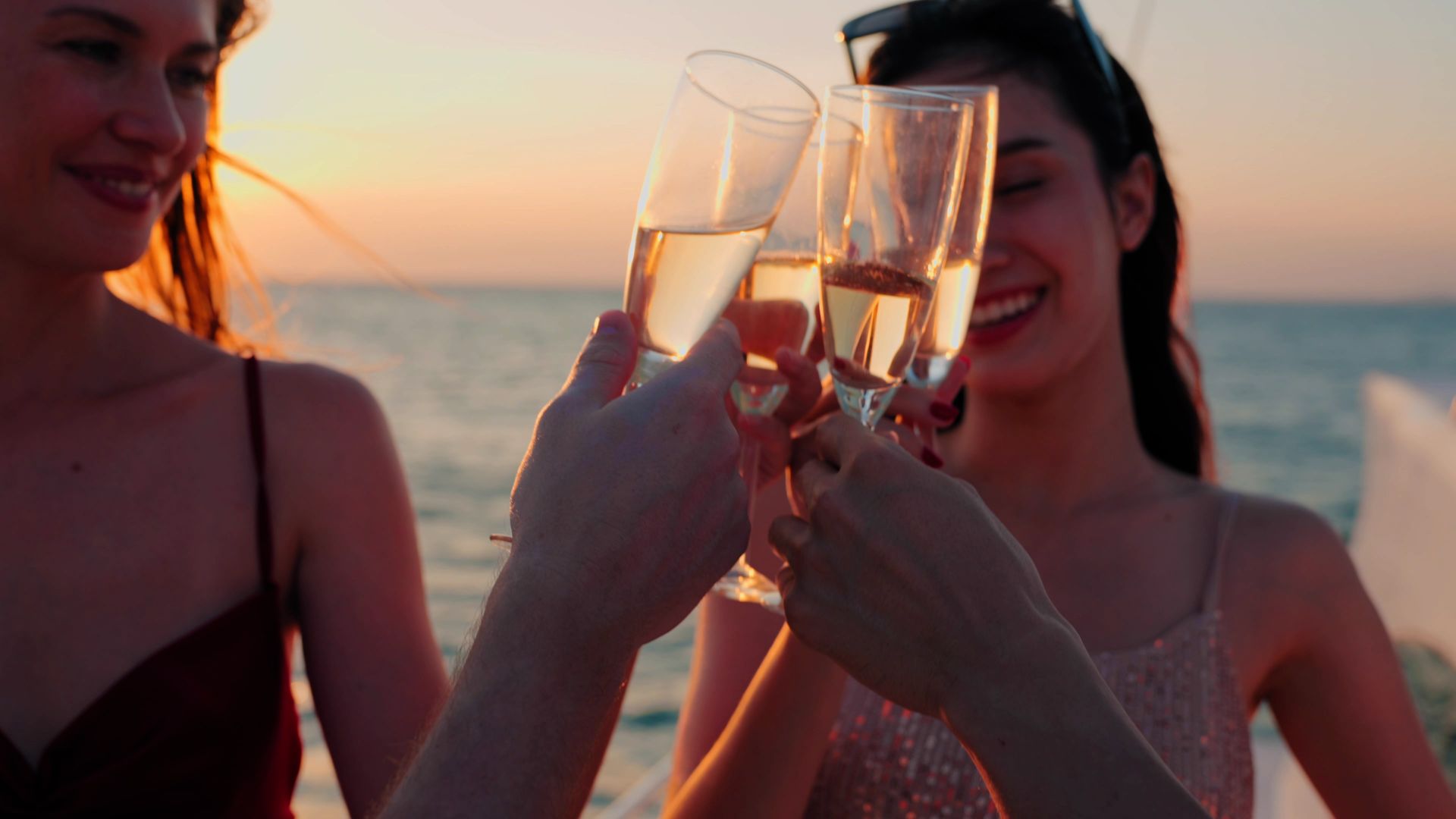 Trois personnes trinquent au champagne au coucher du soleil sur la plage.