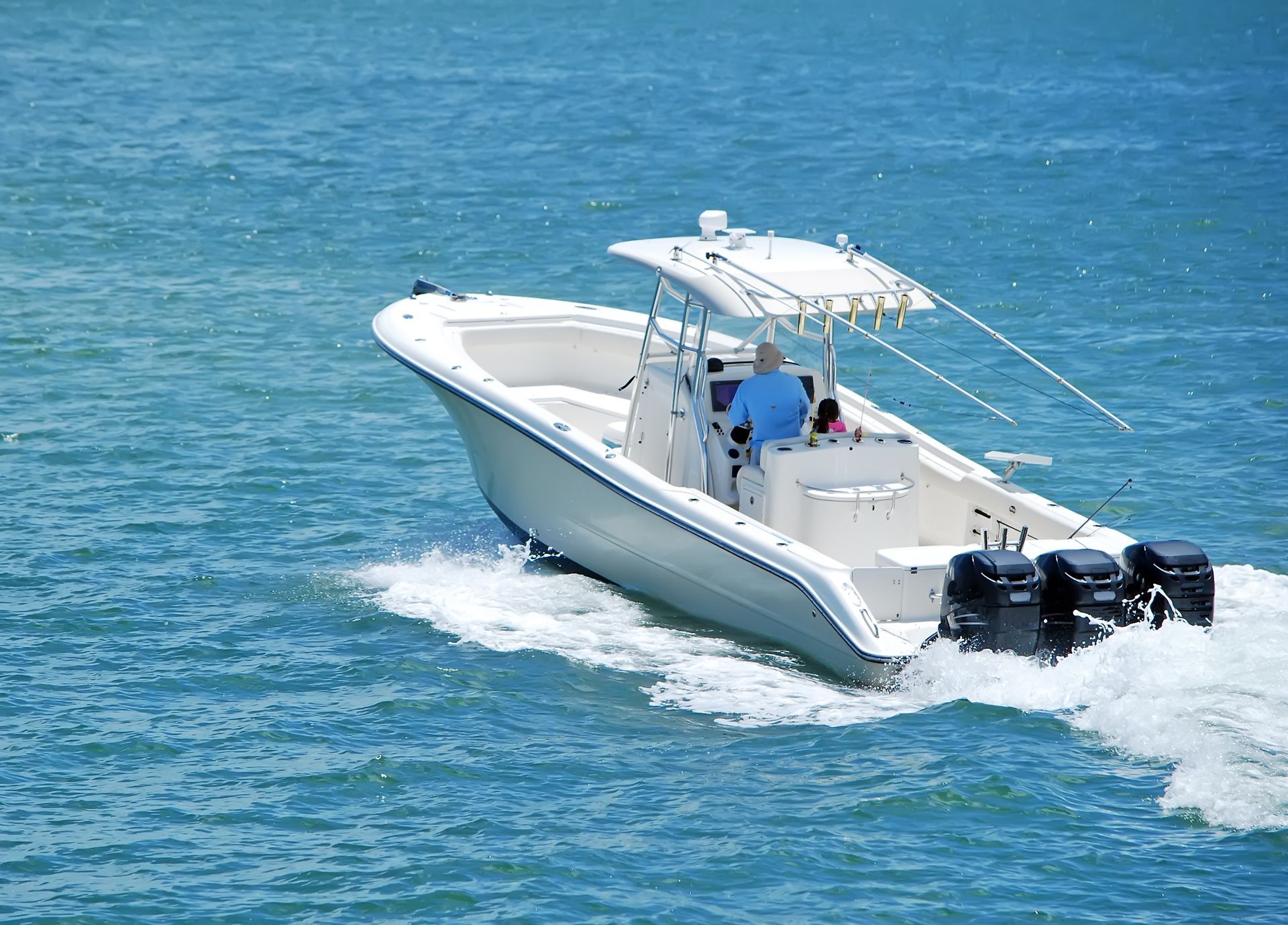 Bateau à moteur blanc filant sur l’eau bleue, avec deux personnes à bord et des moteurs hors-bord visibles