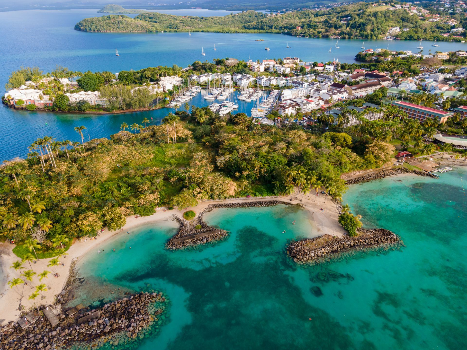 Vue aérienne d’une baie tropicale aux eaux turquoise, avec un littoral rocheux et une ville côtière au loin