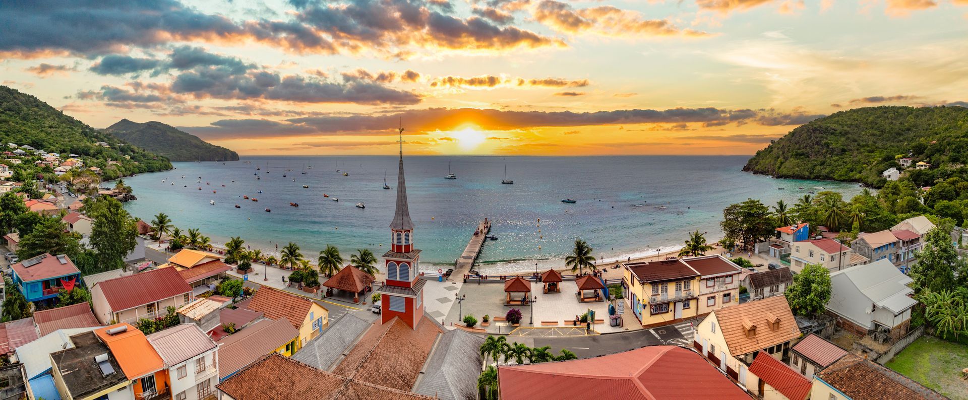 Village côtier coloré et baie au coucher du soleil, avec des maisons aux toits rouges et un clocher au premier plan