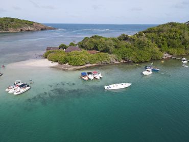 Jetée en bois menant à une baie turquoise où se trouve un petit bateau, avec un village côtier coloré sous un ciel bleu
