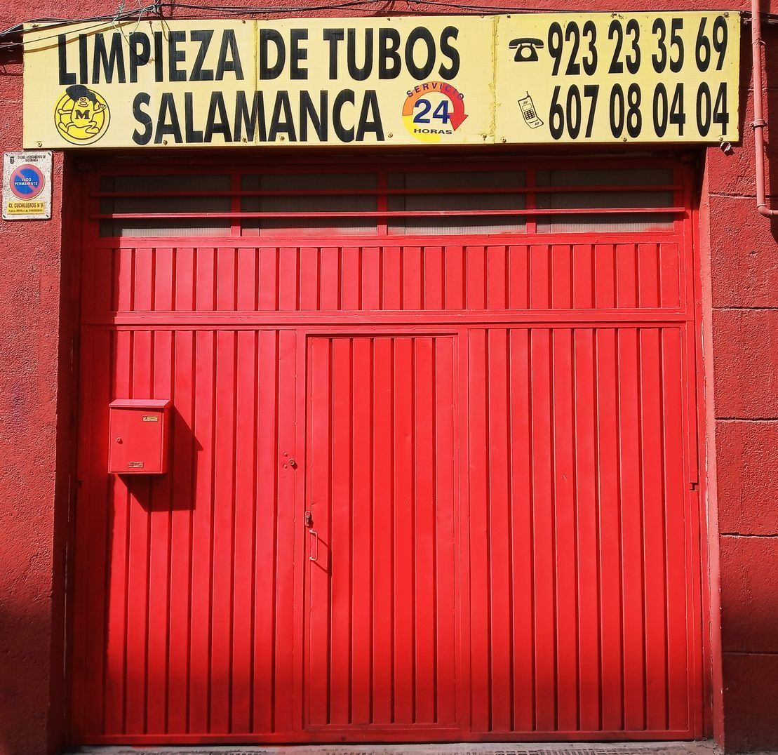 Una puerta de garaje roja con un cartel amarillo encima que dice limpieza de tuberías salamanca