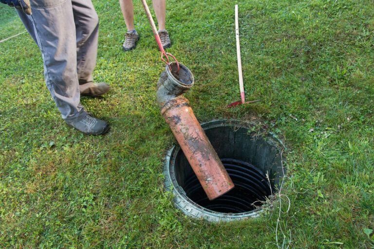 Un hombre está limpiando un tanque séptico con una tubería.