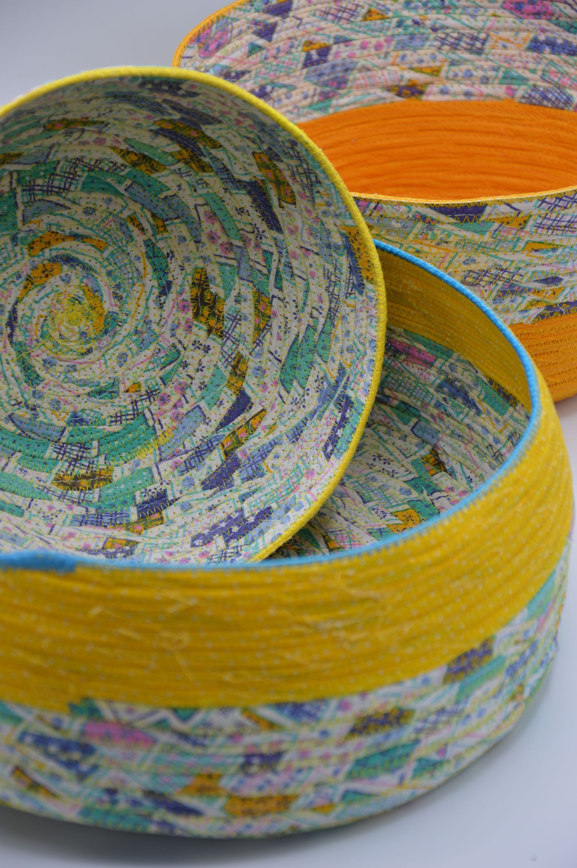 Dos cuencos hechos a mano con tiras de tela enrolladas, con tela colorida y estampada y bordes lisos de color amarillo o naranja.
