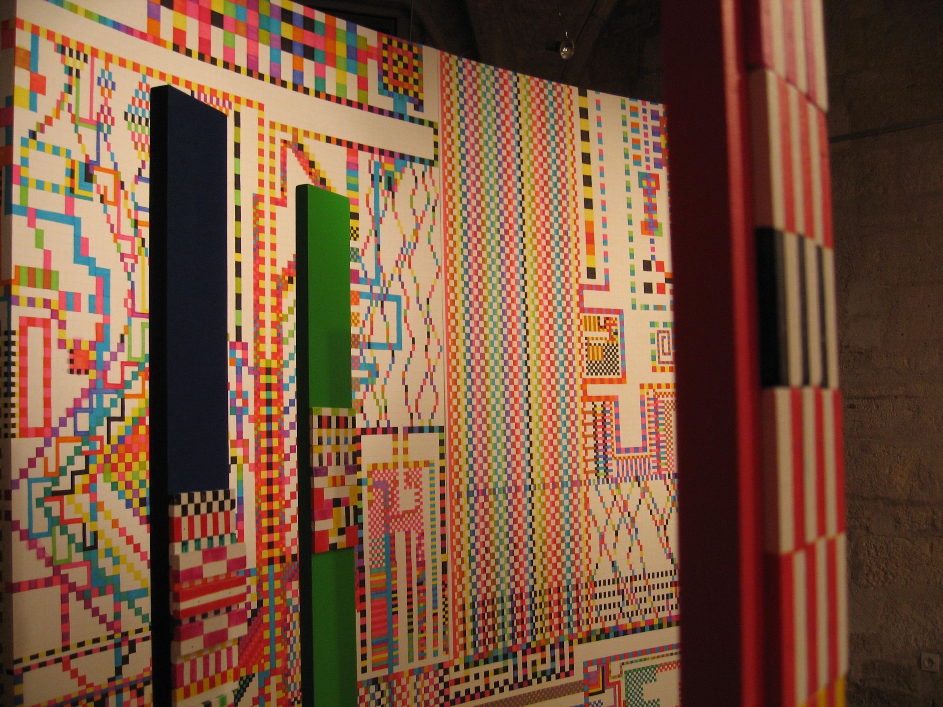 Unos coloridos postes verticales se alzan frente a grandes paneles con intrincados diseños geométricos y líneas.