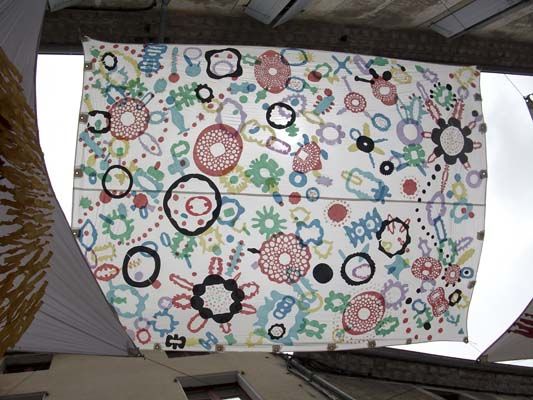 Una gran pancarta rectangular blanca cuelga del techo, decorada con coloridos patrones abstractos de círculos y formas.