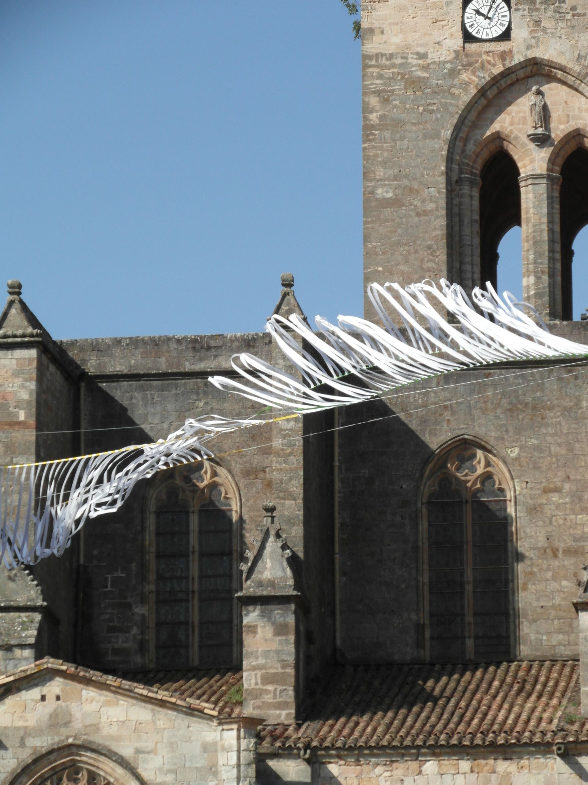 Una gran instalación circular formada por numerosos tubos azules colgantes, suspendida en un bosque bajo un cielo brillante.