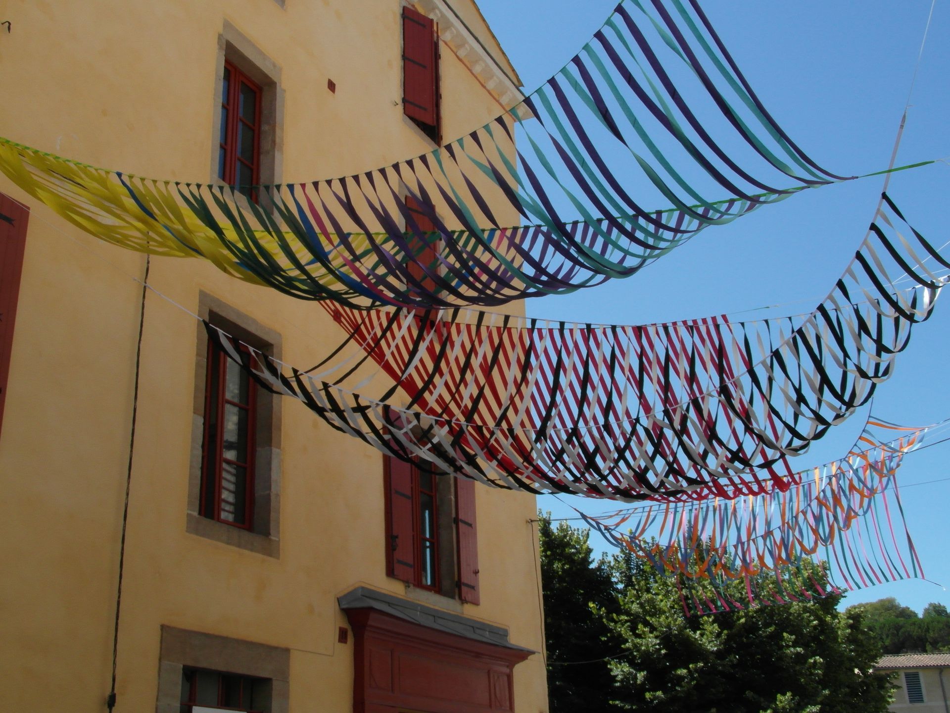 Cintas multicolores cuelgan formando guirnaldas festivas sobre un fondo de árboles verdes.