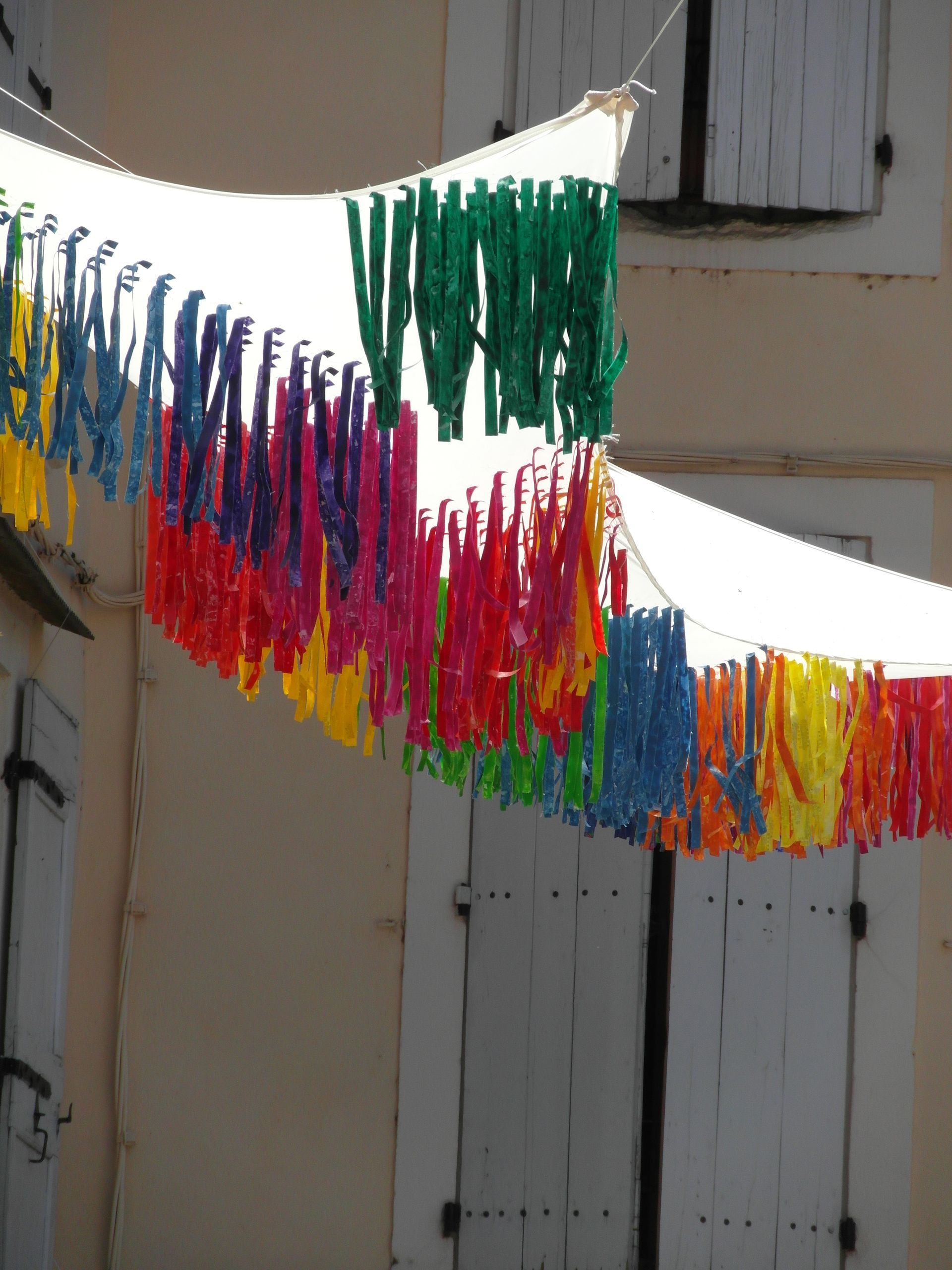 Cintas de tela de colores cuelgan de toldos blancos que se extienden entre los edificios.