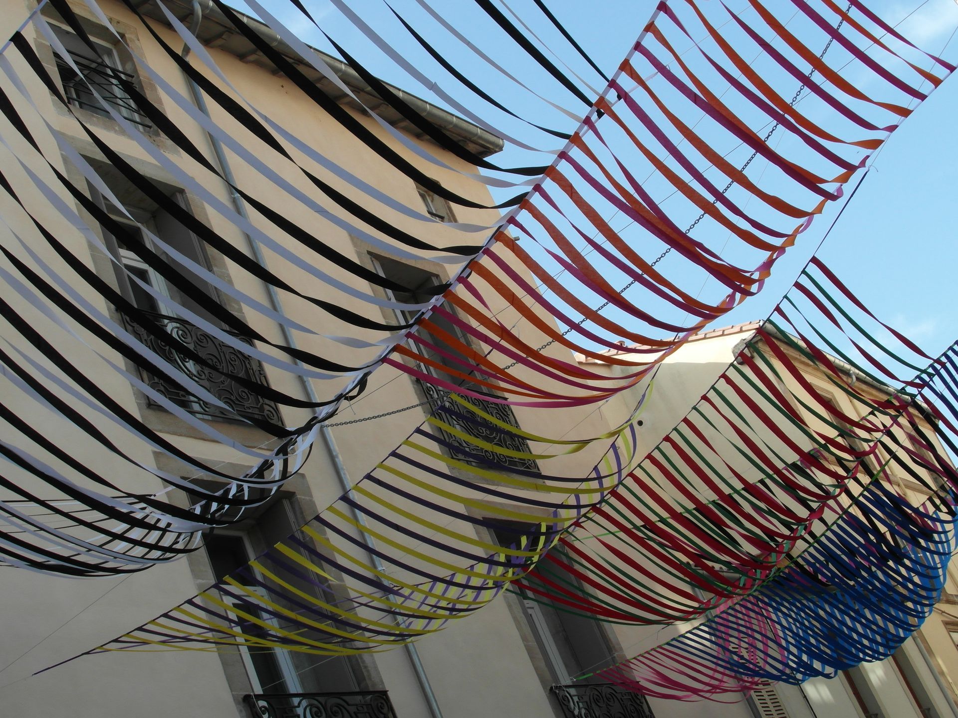 Cintas de colores cuelgan entre dos edificios, creando un dosel decorativo contra el cielo azul.