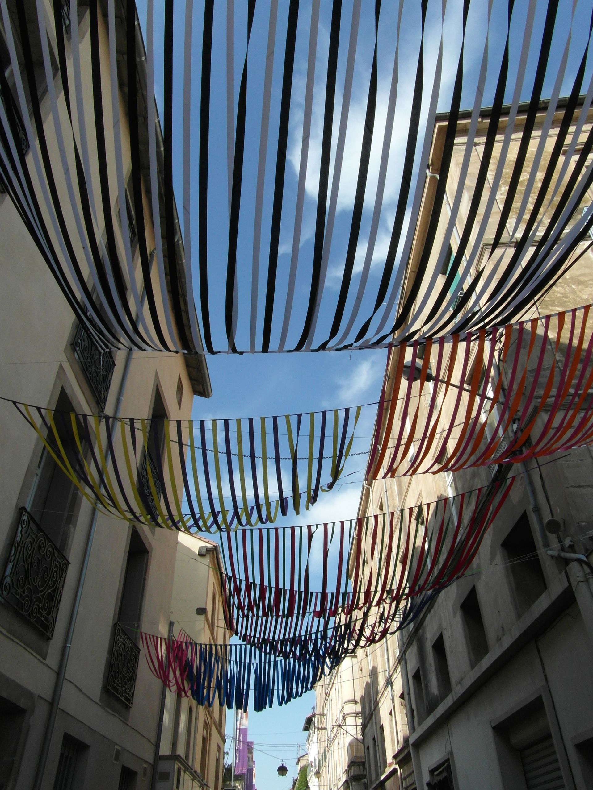 Cintas coloridas de diversos diseños se extienden a lo largo de una calle estrecha entre edificios altos, enmarcando un cielo azul brillante.