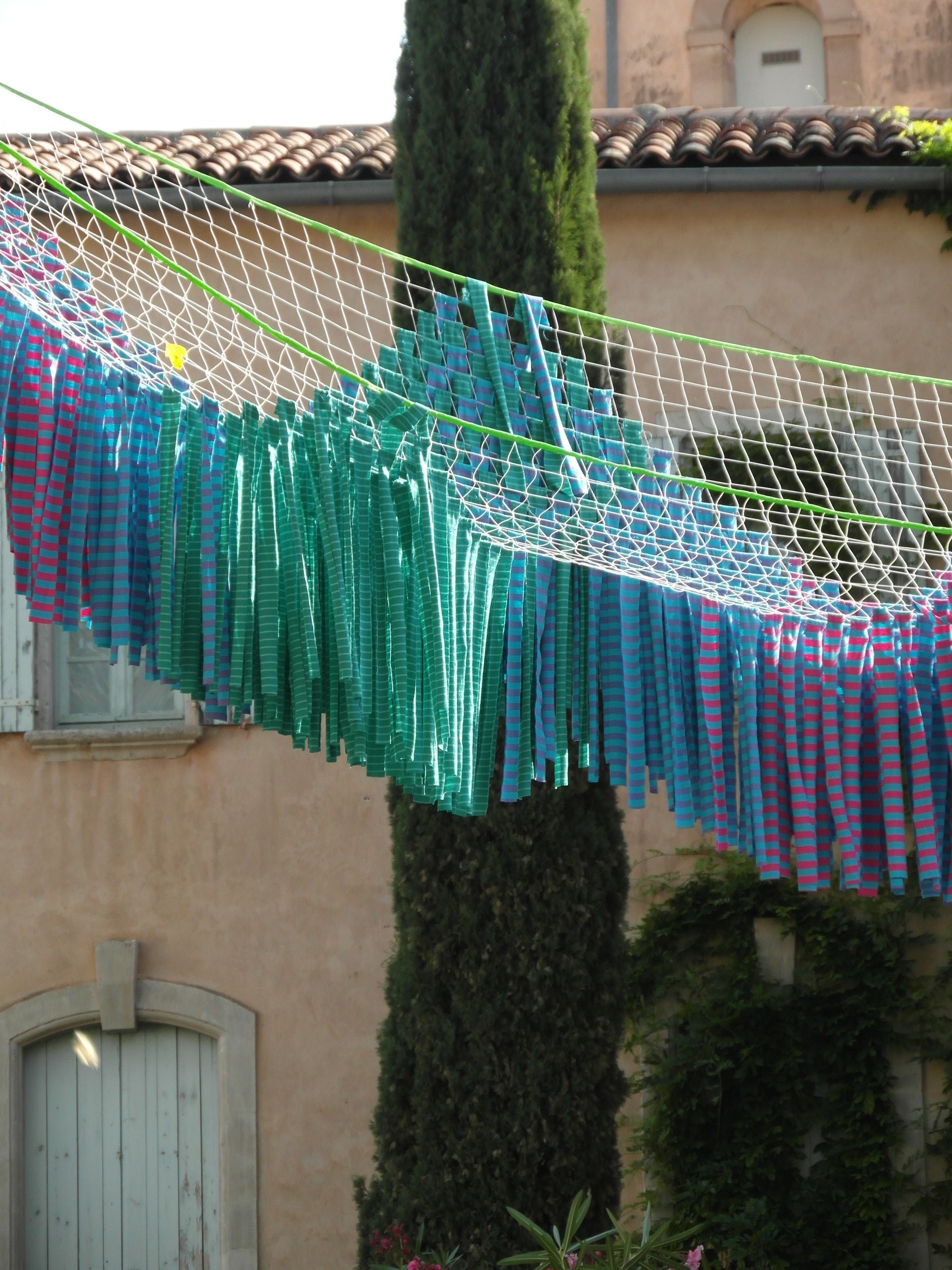 Una red decorativa colgaba con tiras de tela multicolores en tonos morados, azules y verdes, frente a un edificio de piedra.