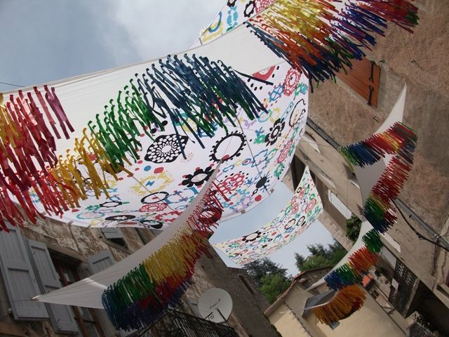 Pancartas coloridas con diseños abstractos cuelgan sobre un letrero de la calle anunciando el festival de poesía Voix de la Méditerranée.