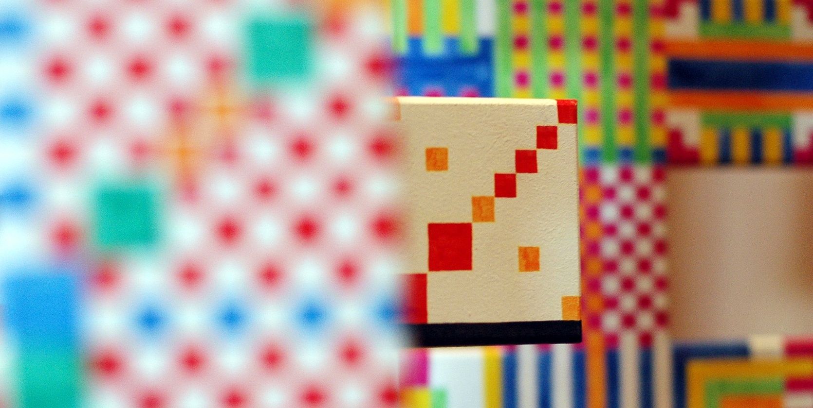 Una escultura con patrones geométricos de colores vivos y pequeños recortes cuadrados sobre un fondo de pared de piedra.