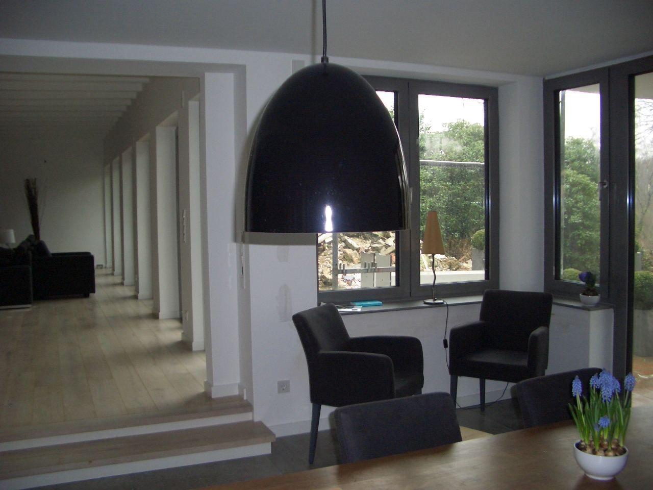 Modernes Wohnzimmer mit schwarzen Sesseln, großer Pendelleuchte und bodentiefen Fenstern mit Blick nach draußen