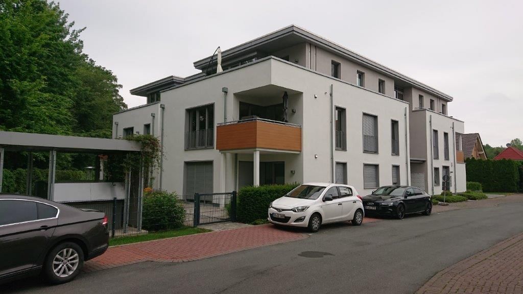 Neues Mehrfamilienhaus im Bau, mit weißer Fassade und Balkonen; zwei Gestalten stehen draußen.