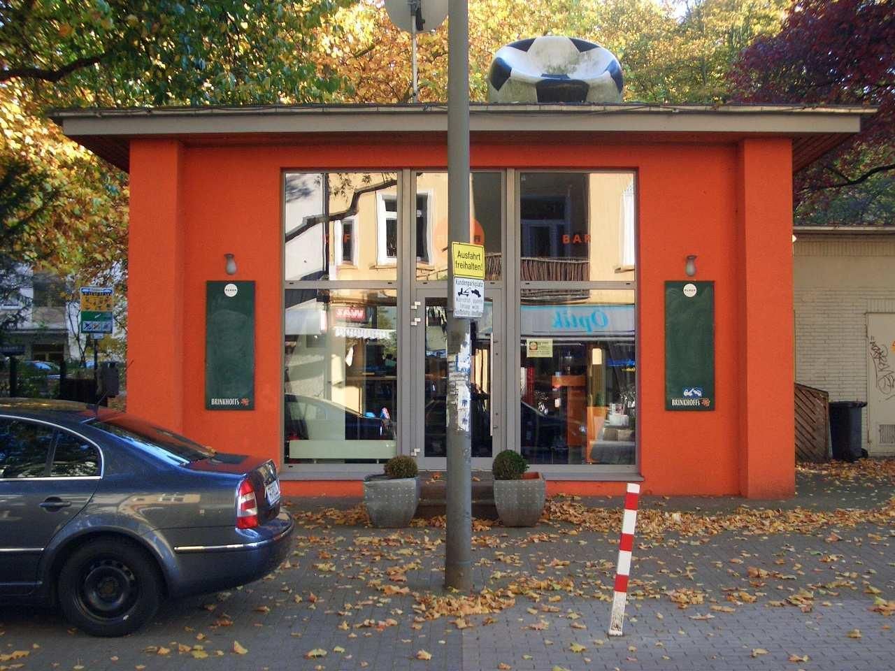 Orangefarbenes Gebäude mit einem großen Fußball auf dem Dach. Ein silbernes Auto parkt davor.