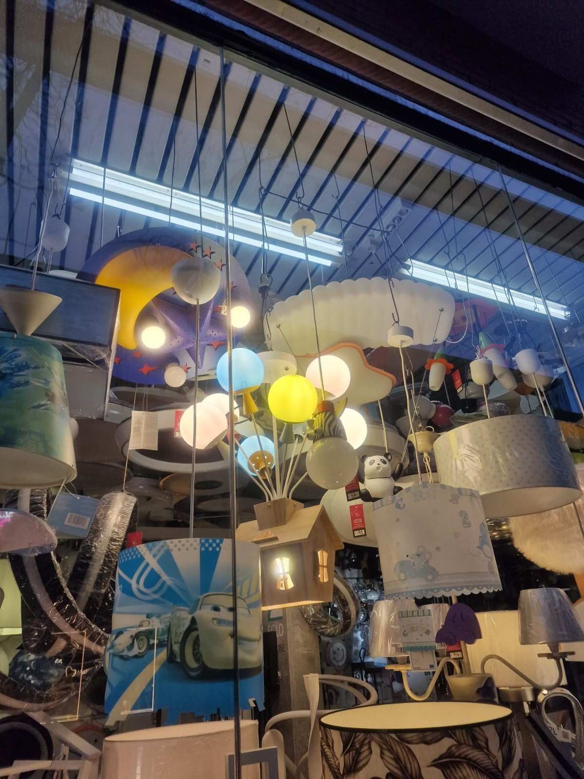 Un escaparate repleto de coloridas lámparas decorativas, entre ellas una lámpara con forma de casa adornada con globos.