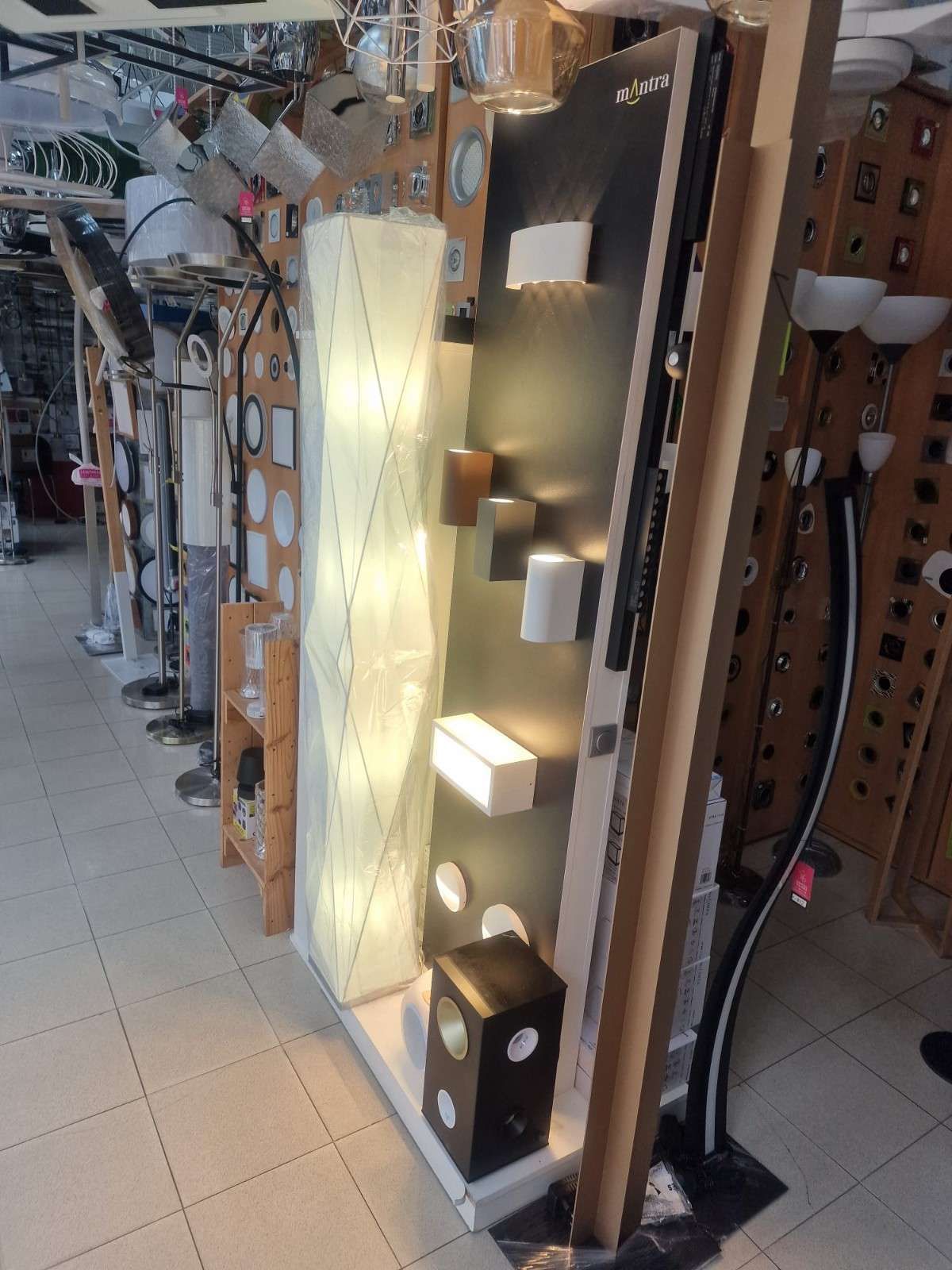 Un expositor en una tienda de iluminación que muestra varias lámparas de pared y una lámpara de pie alta y texturizada.