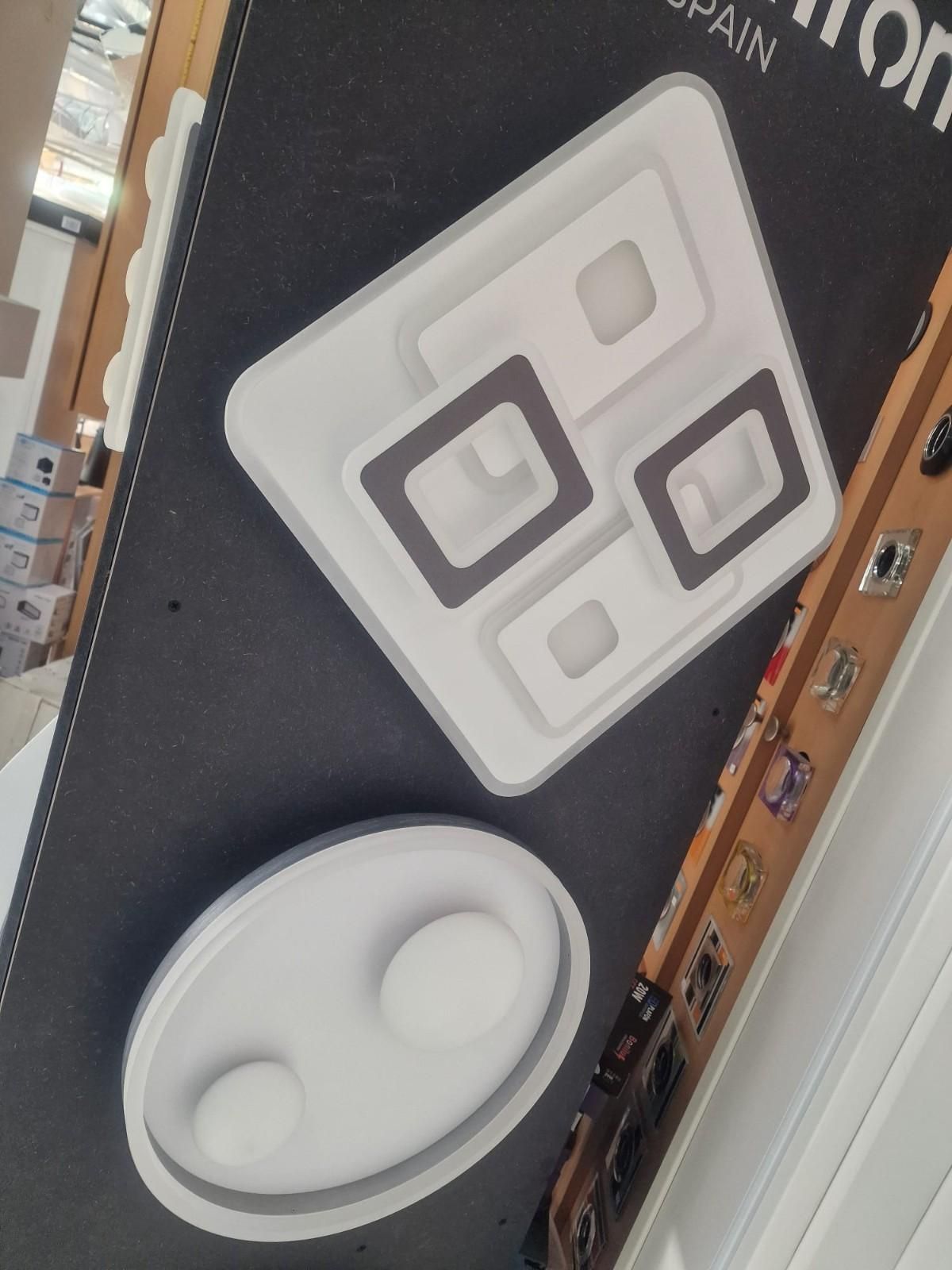 Dos modernas lámparas de techo minimalistas expuestas sobre un panel de fondo oscuro en una tienda.