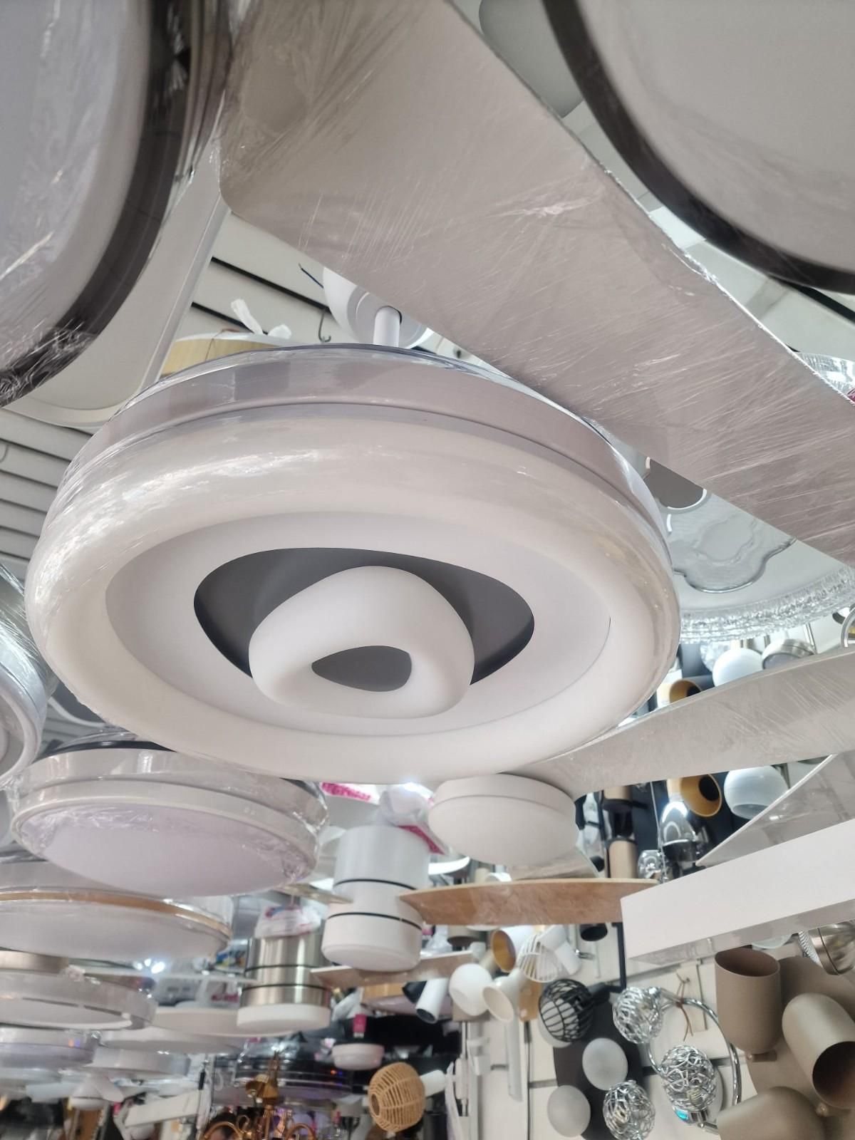 Un moderno ventilador de techo circular blanco con luz, expuesto en una tienda de iluminación.