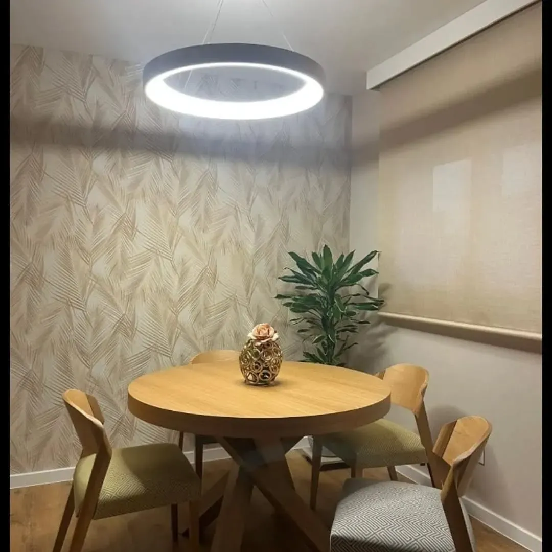 Un conjunto de comedor con una mesa redonda de madera y cuatro sillas, iluminado por una gran lámpara colgante