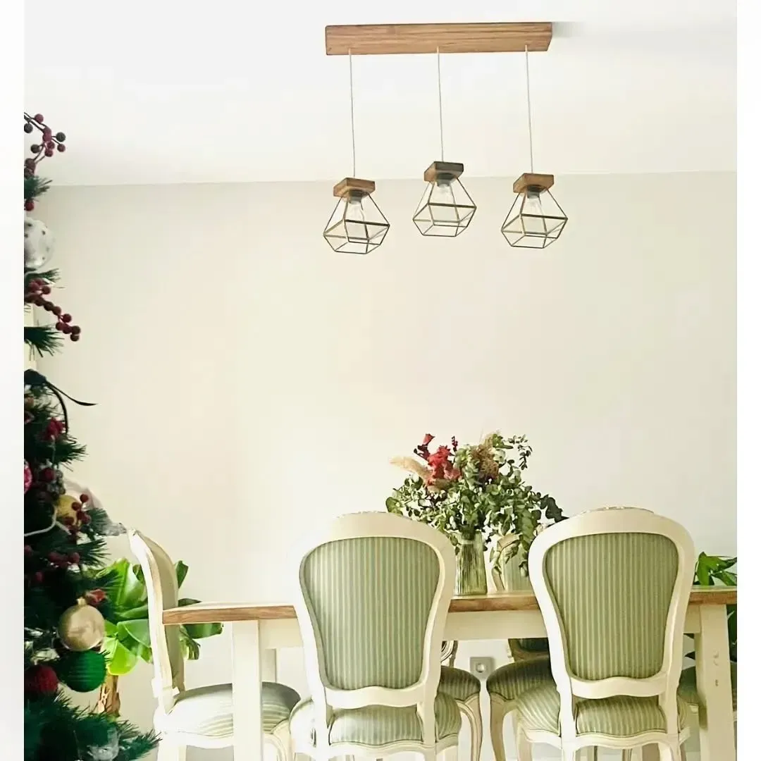 Un comedor con una mesa de madera, tres sillas tapizadas de color verde salvia y un trío de lámparas colgantes geométricas.