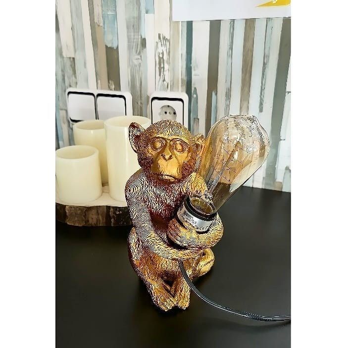 Una figurita metálica de color dorado con forma de mono que sirve de base para una lámpara